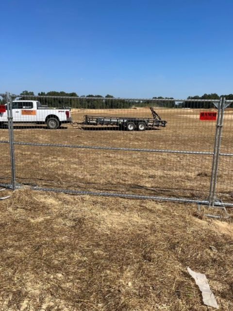 A truck and trailer are parked in a field behind a fence.