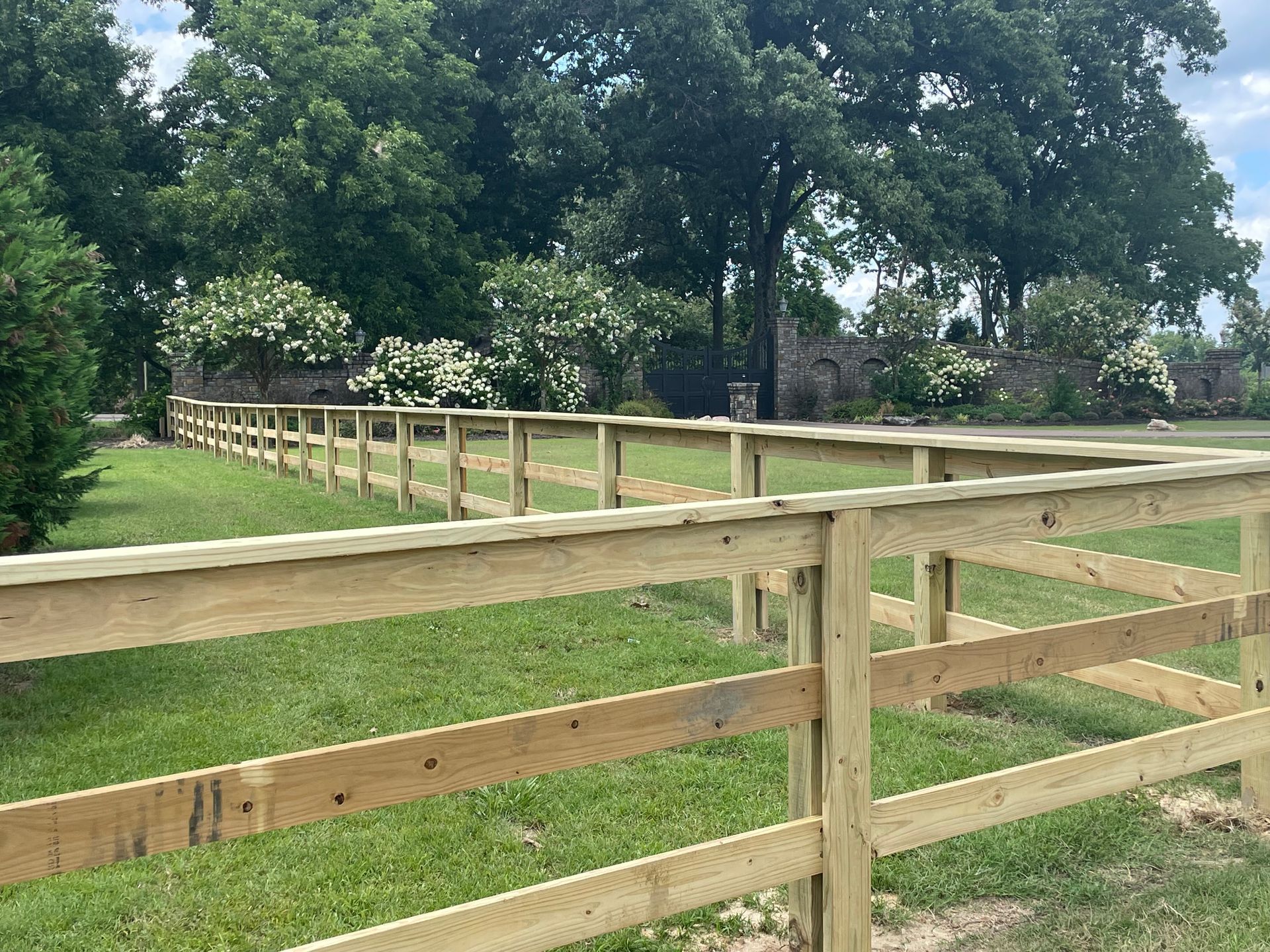 A wooden fence surrounds a grassy field with trees in the background.