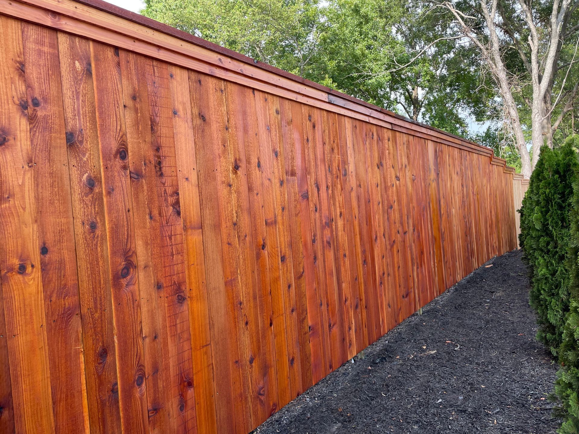 A wooden fence is surrounded by trees and gravel.