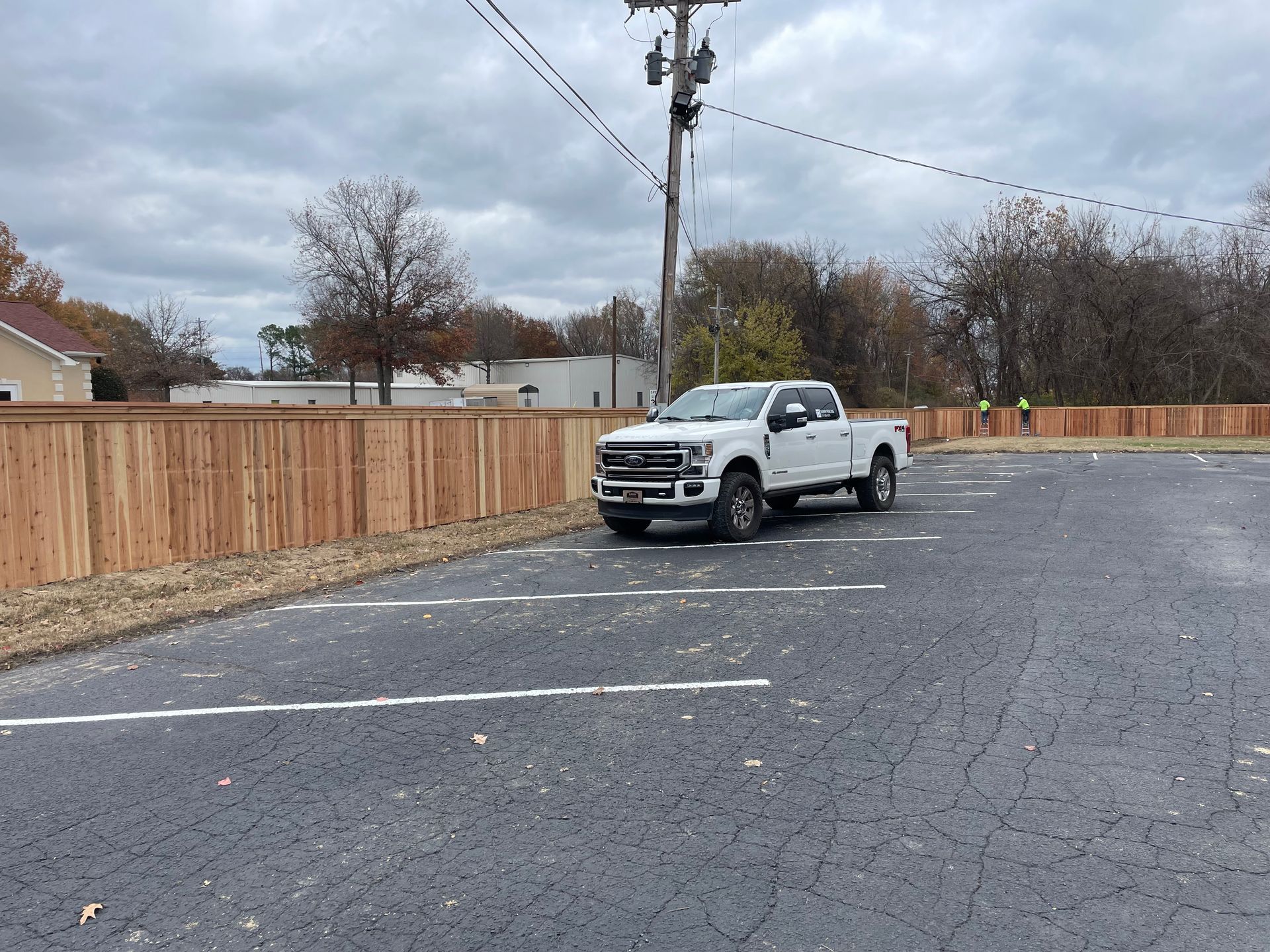 A white truck is parked in a parking lot next to a wooden fence.