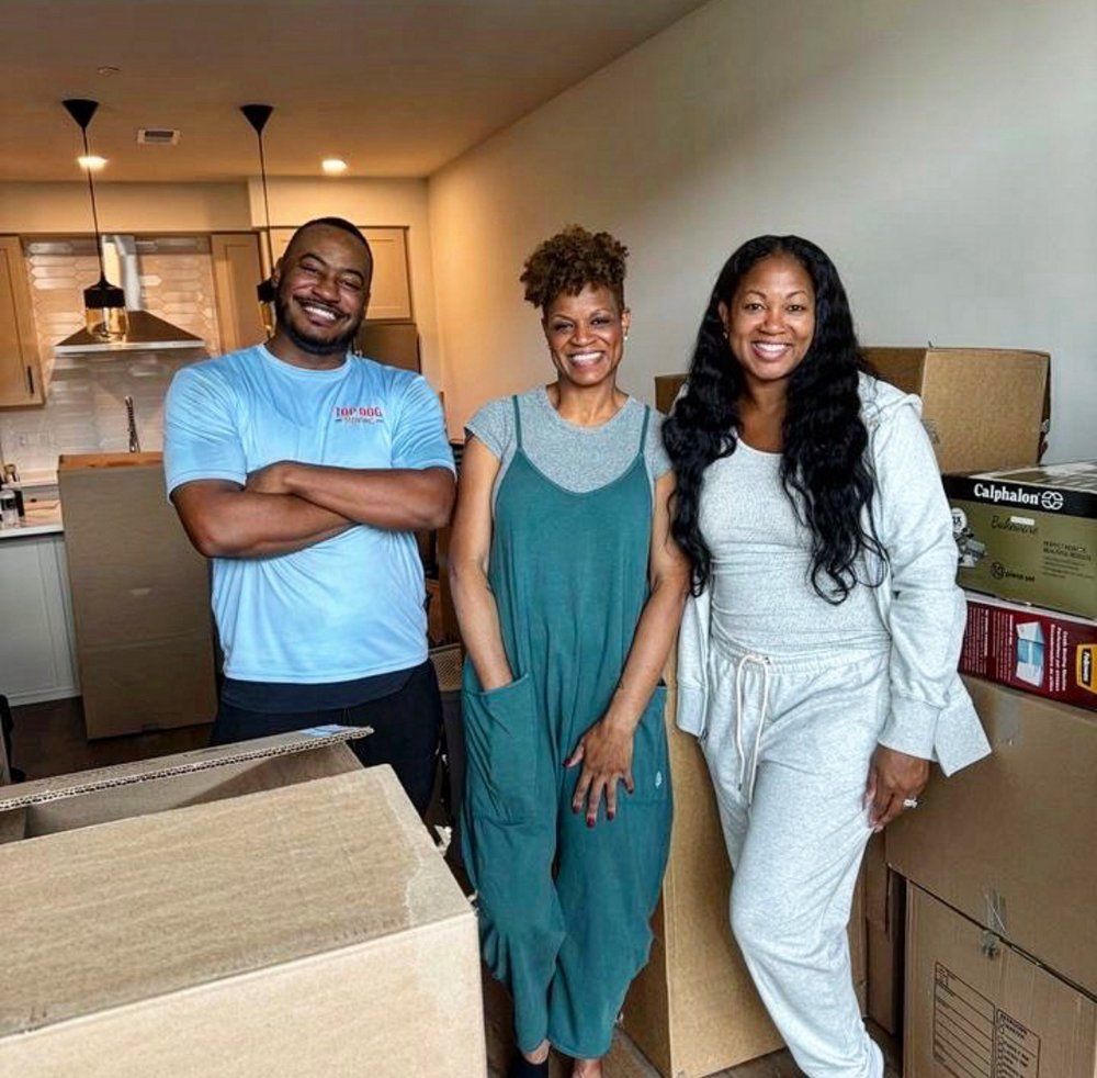 A man and two women are standing next to each other in a room filled with cardboard boxes.