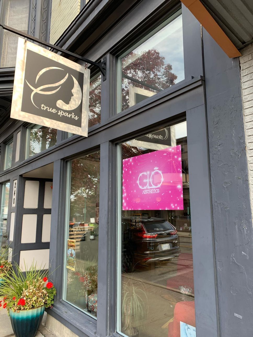 Storefront with black-and-white sign and bright pink window poster beside a flower planter