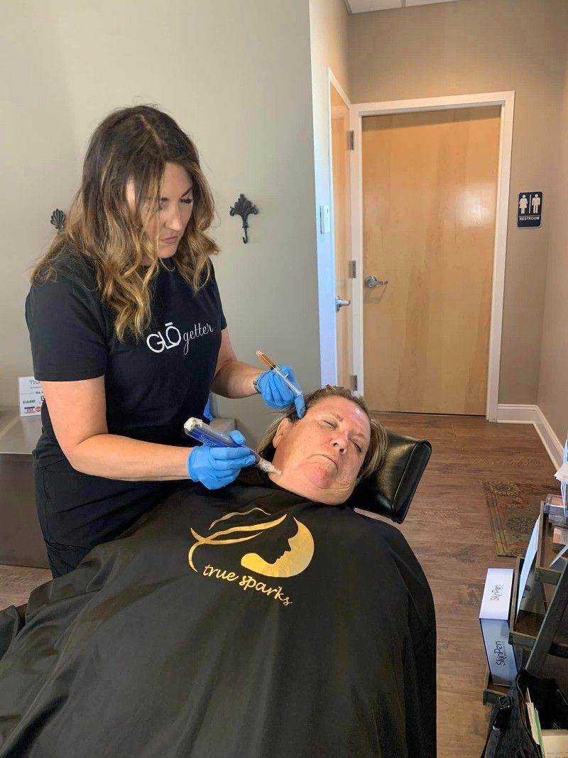 Woman receiving cosmetic treatment on her face. Another woman in blue gloves performs the procedure in a clinic.