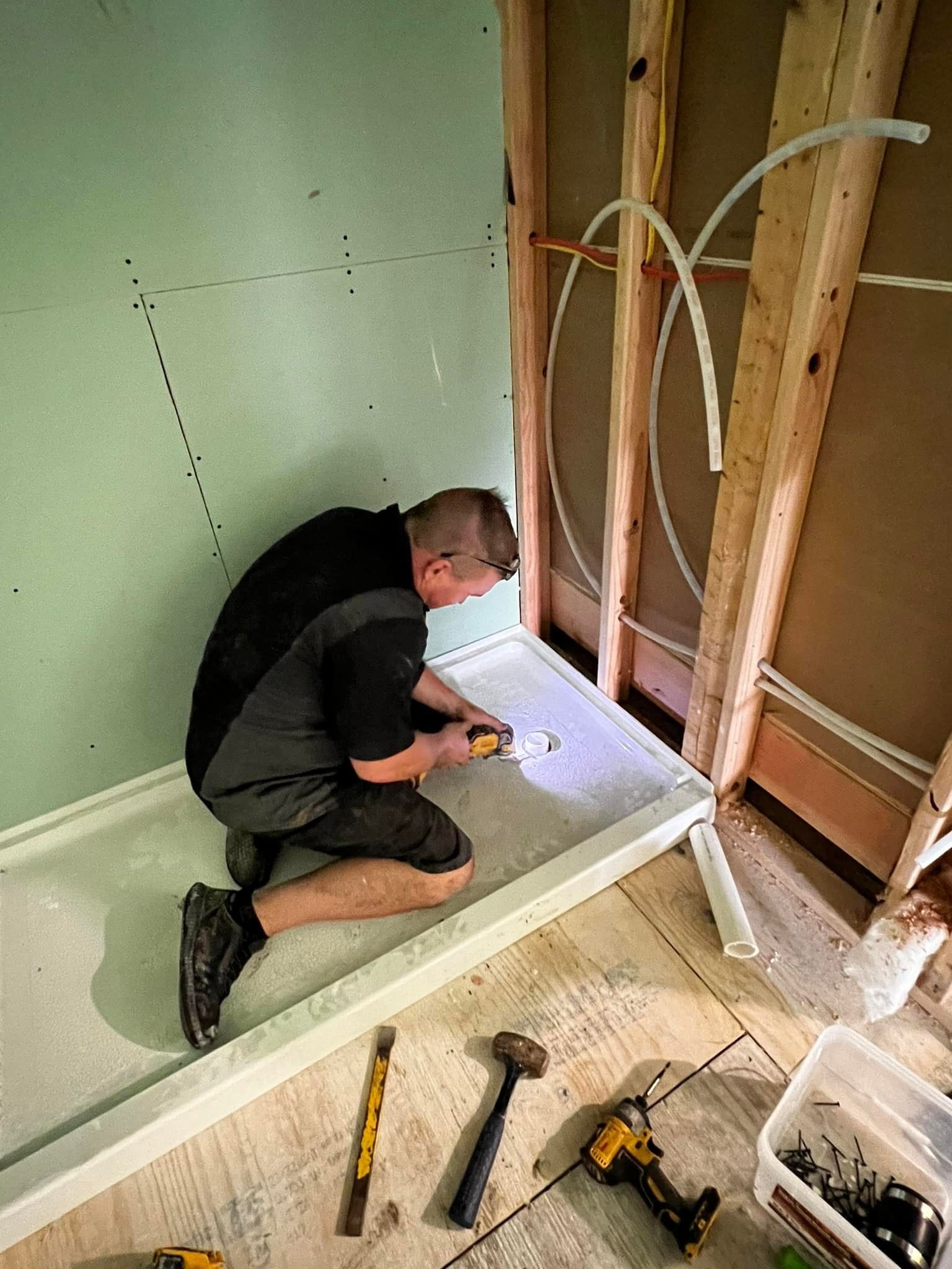 A man is kneeling down in a bathroom while working on a shower stall.
