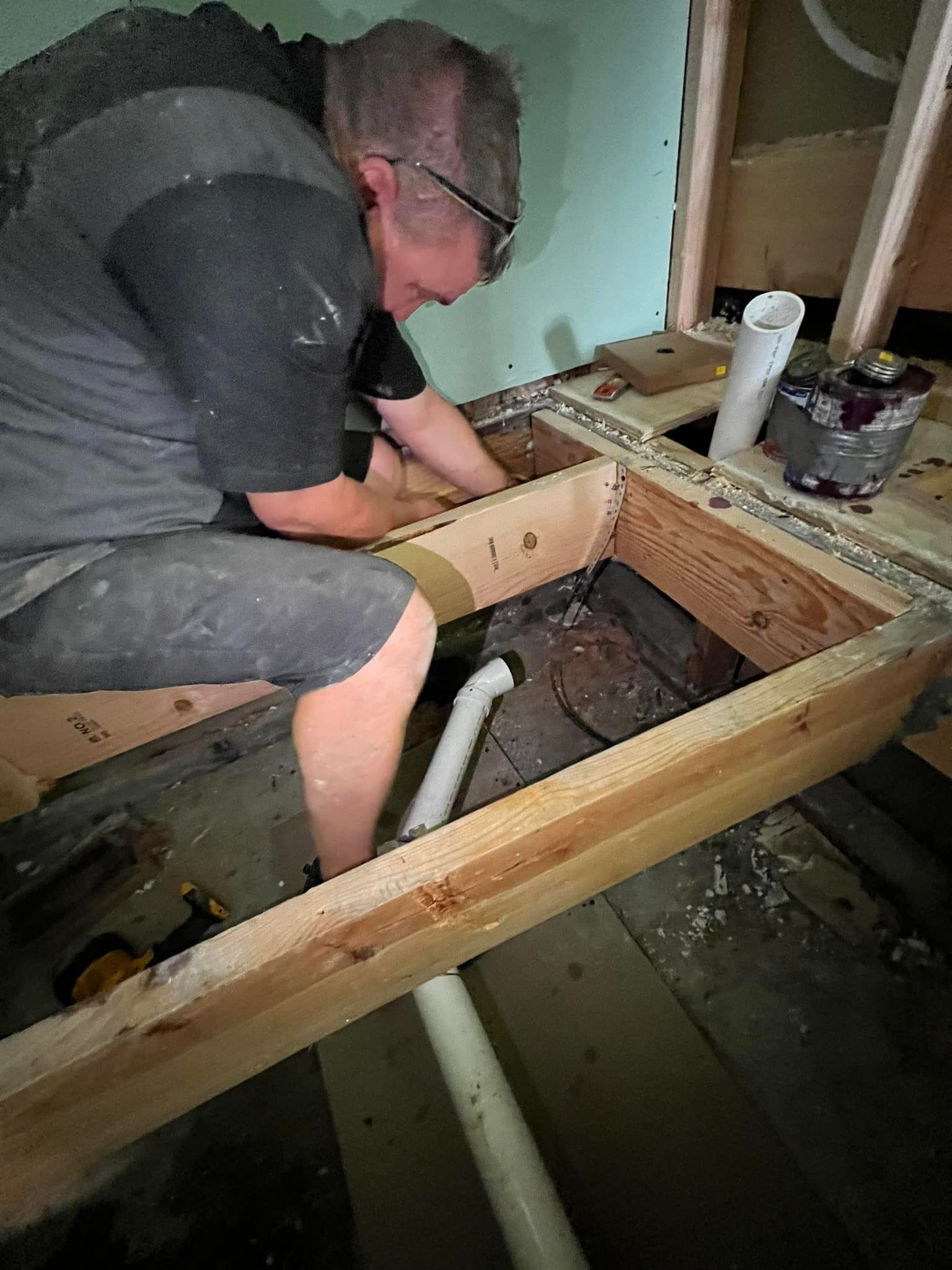 A man is kneeling down in a wooden box working on a pipe.