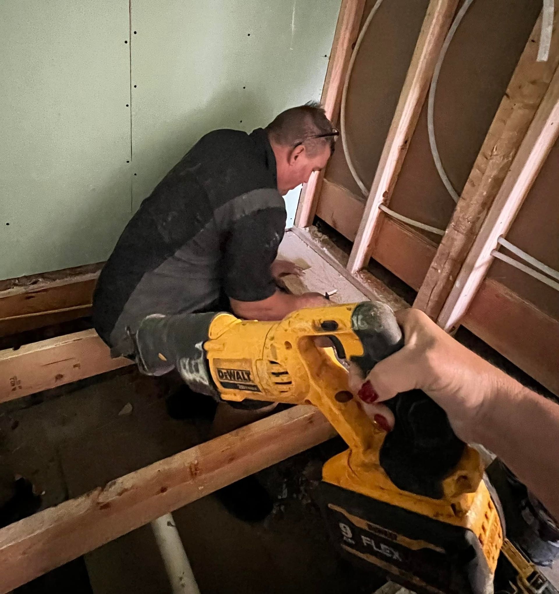 A man is kneeling down in a wooden box working on a pipe.
