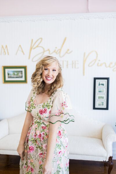 A woman in a floral dress is standing in front of a white couch.