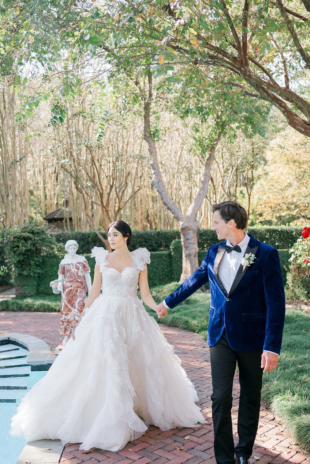 A bride and groom are walking next to a pool holding hands.