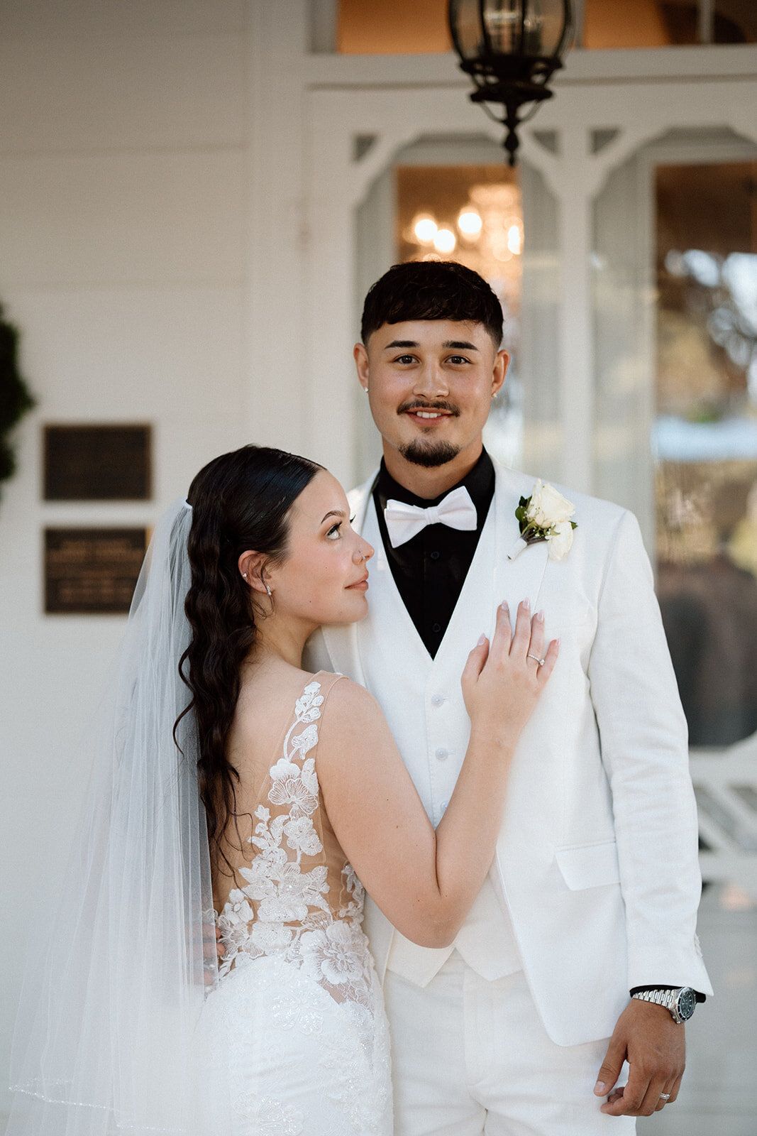 A bride and groom are posing for a picture in front of a white building.