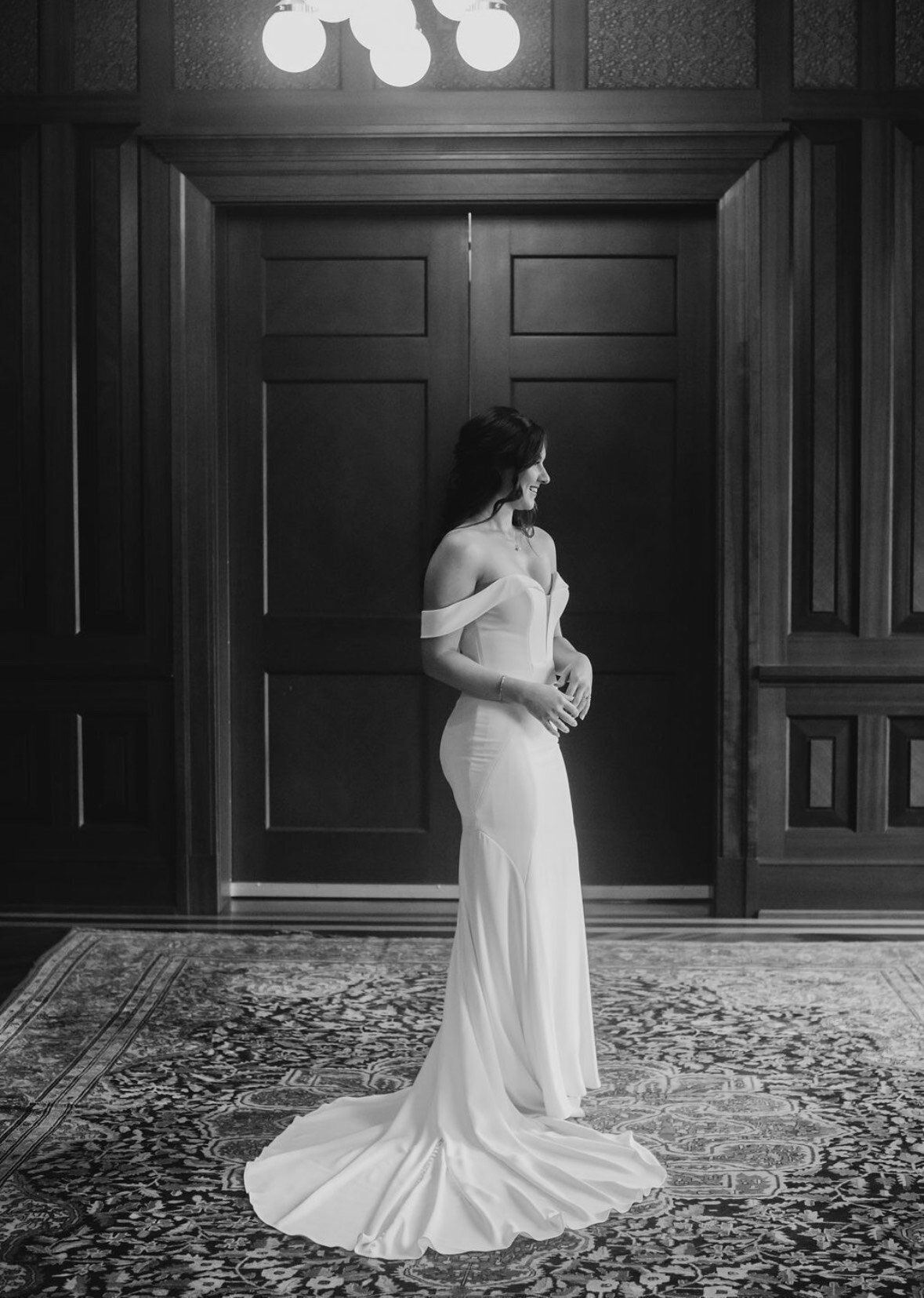 A black and white photo of a woman in a wedding dress standing in front of a door.