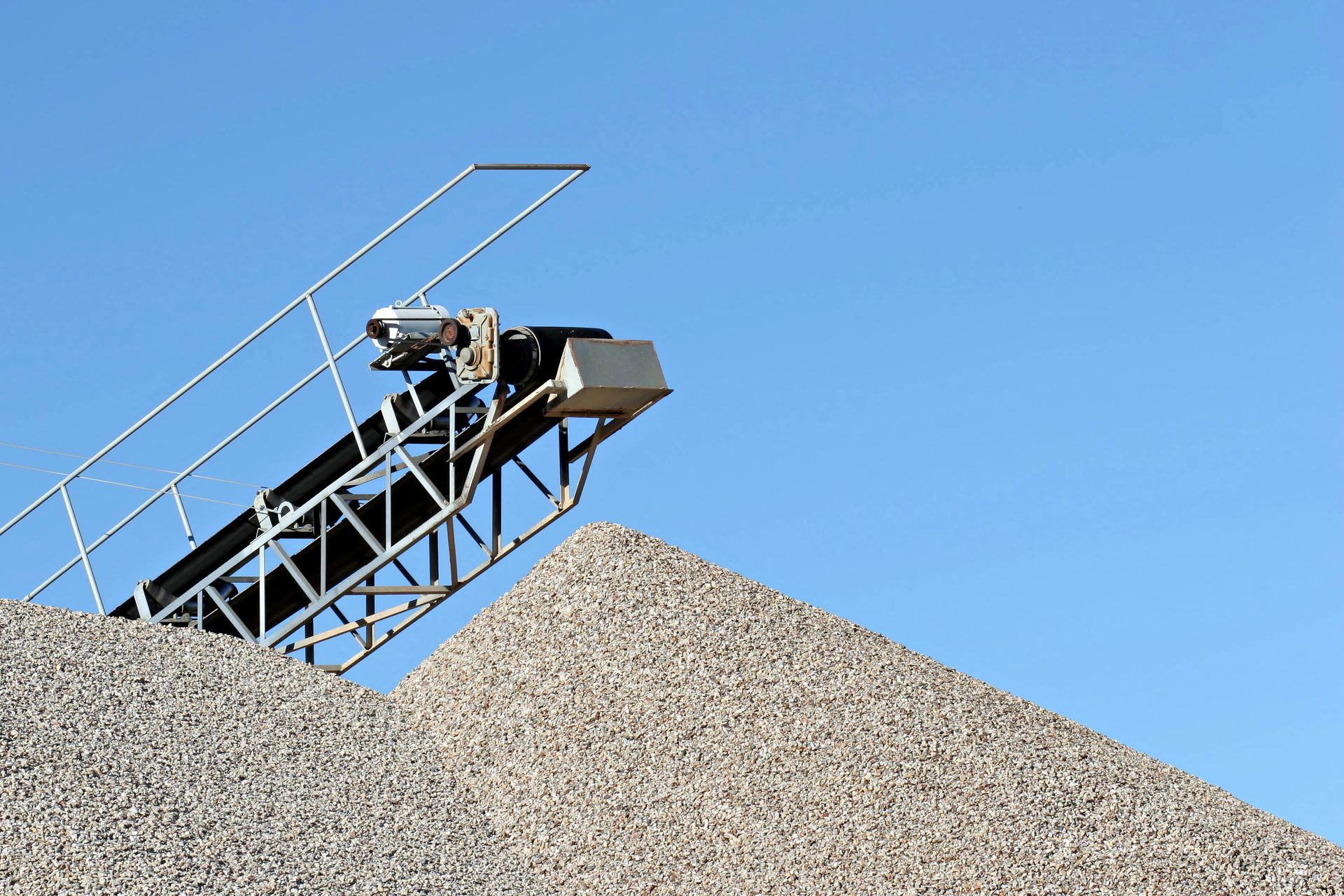 Conveyor belt unloading gravel onto a large pile under a clear blue sky