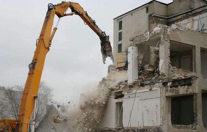 Excavator demolishing a concrete building, with dust and broken walls