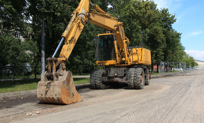 Yellow excavator parked on a gravel road with its bucket resting on the ground near trees.