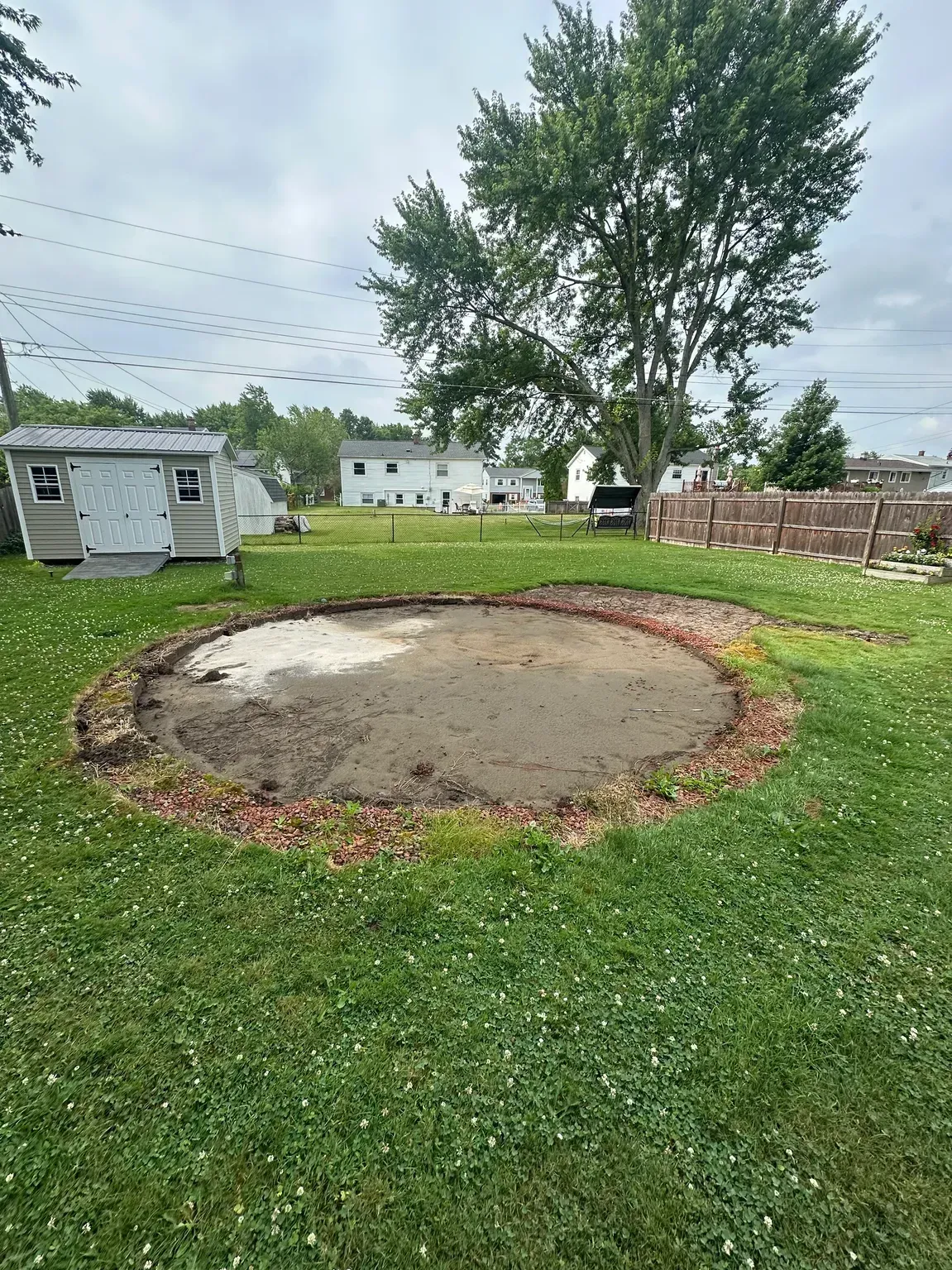 Backyard with a circular fire pit ring and a small shed, grassy yard, and a tree in the background