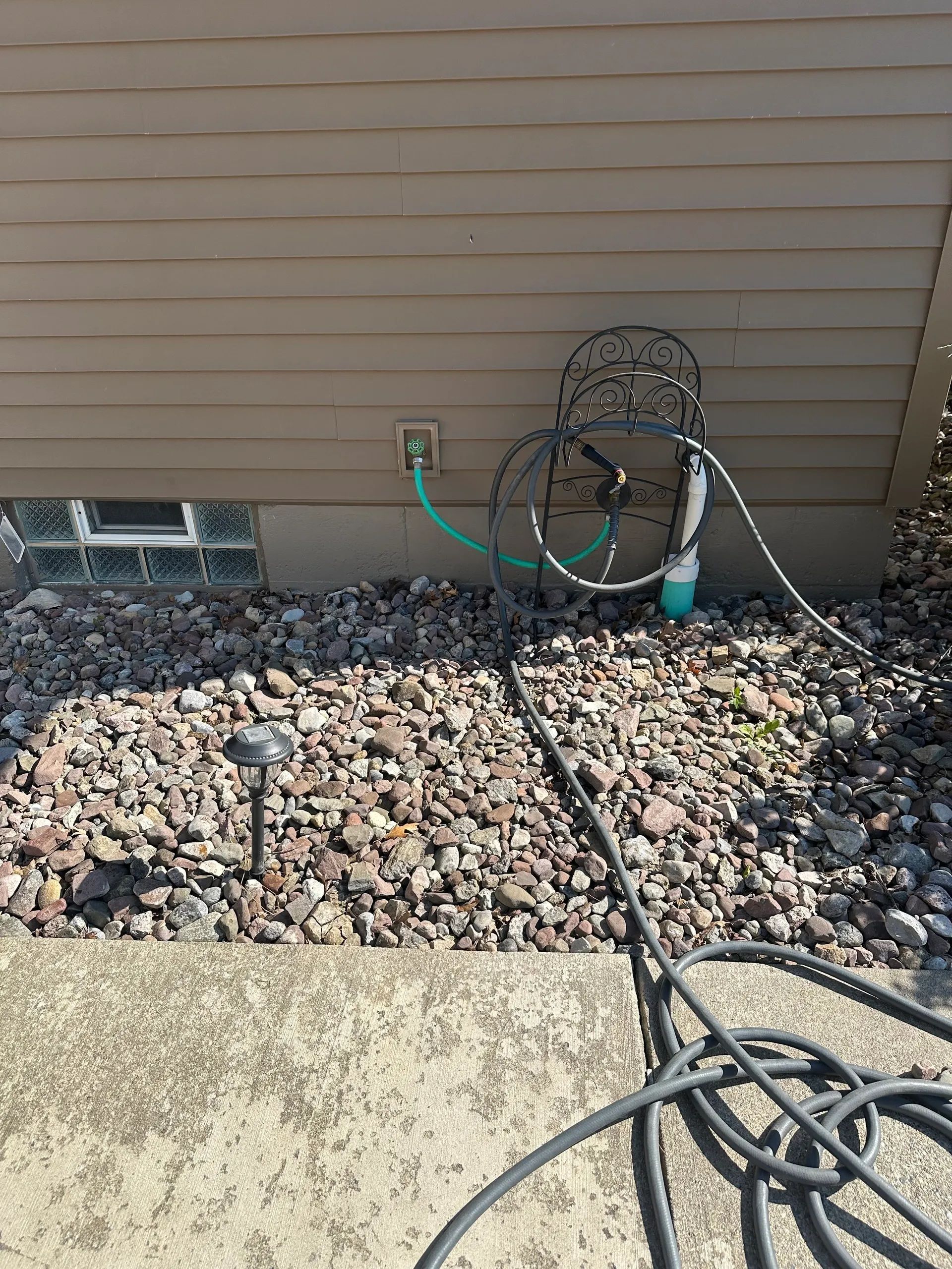 Exterior wall with coiled hoses and cables beside a rock-covered yard.