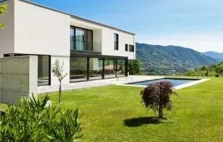 Modern white house with large windows overlooking a green lawn and distant mountains.