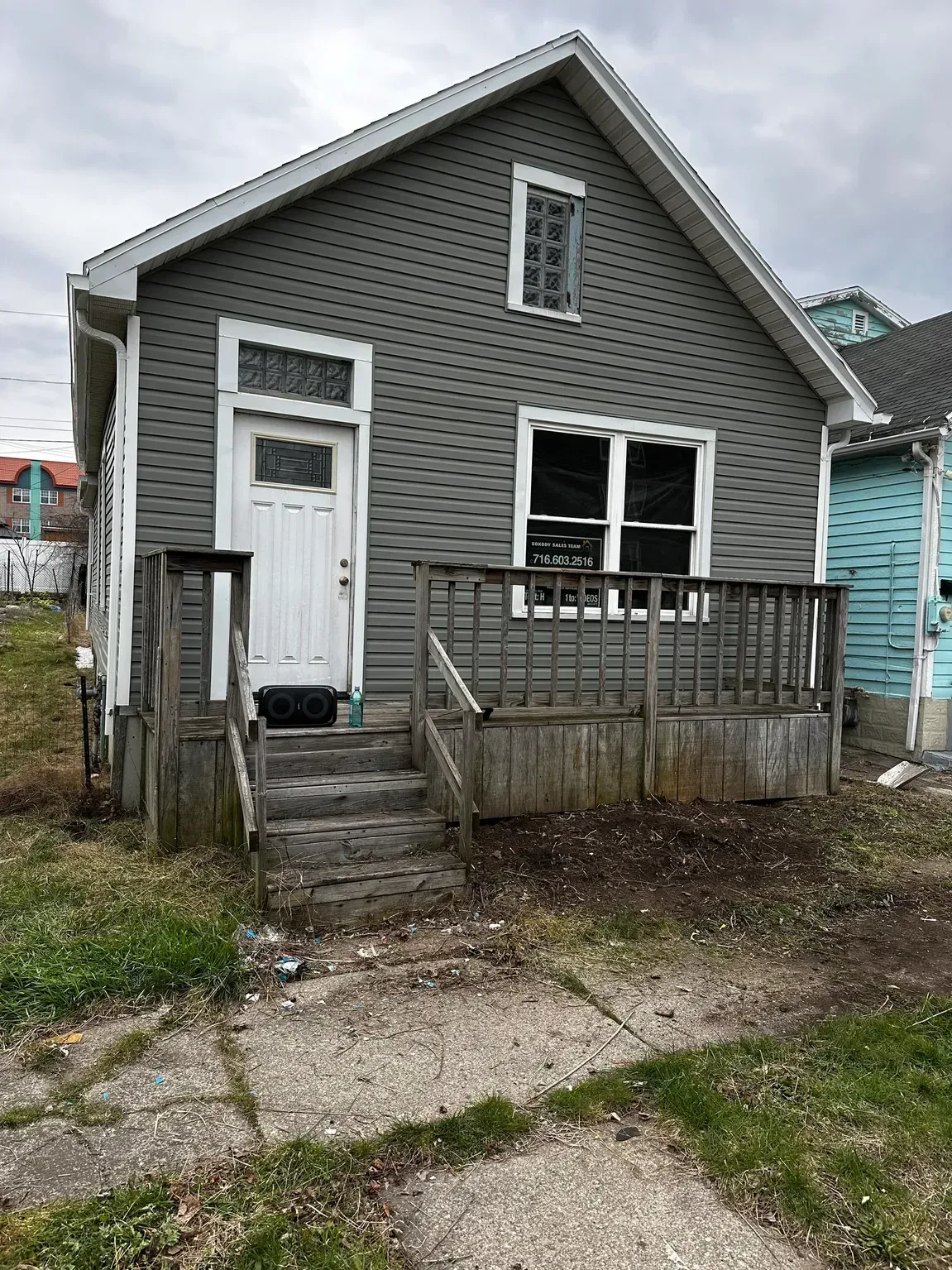 Small gray house with white trim, front steps, and a weathered porch in a residential neighborhood