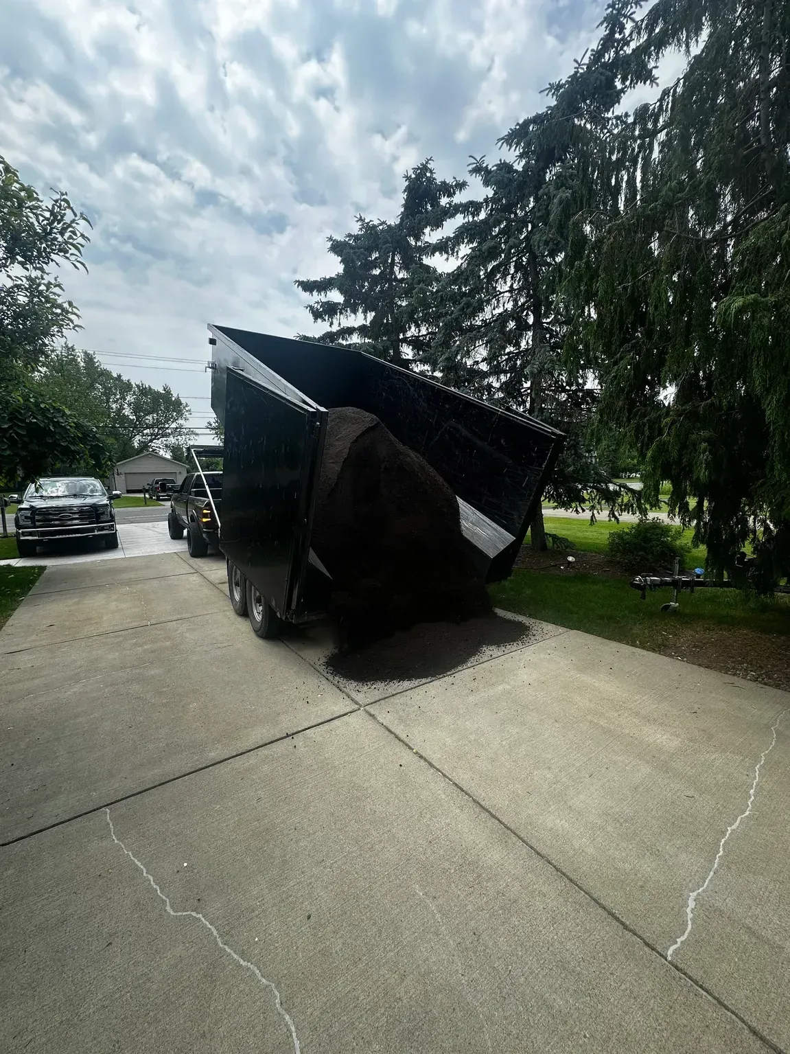 Overturned black tarp-covered object on a driveway beside trees and parked cars