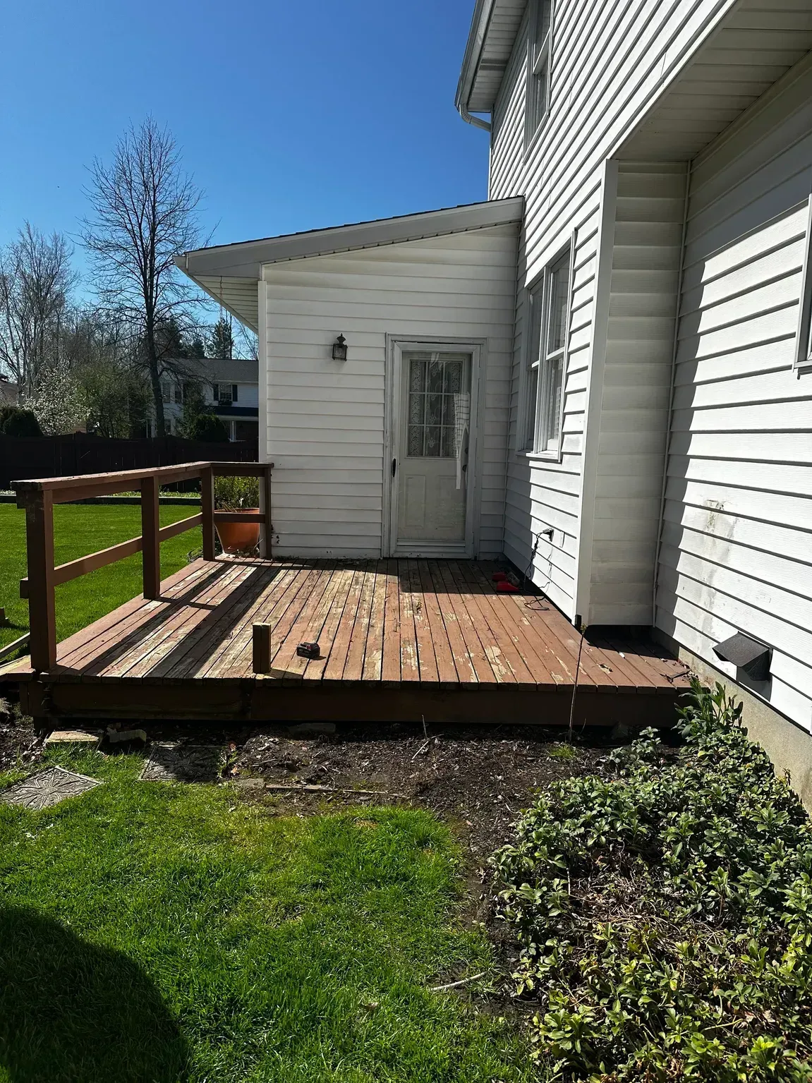 Back deck with wooden railing, small white shed, and house siding on a sunny day