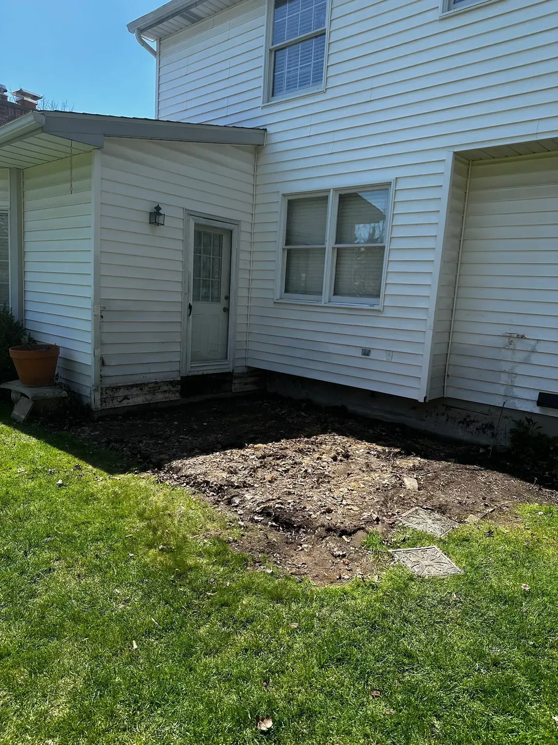 White house exterior with a small entry porch and a bare dirt patch beside a grassy lawn