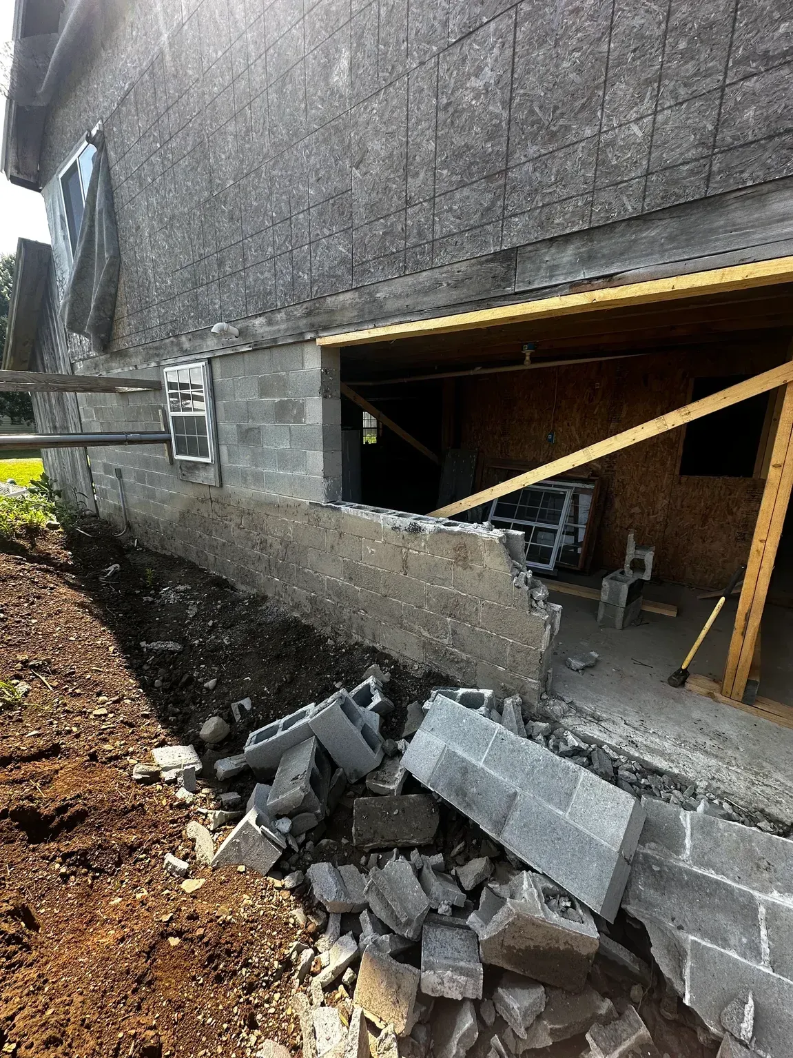Collapsed concrete wall with debris piled beside a basement opening under a building