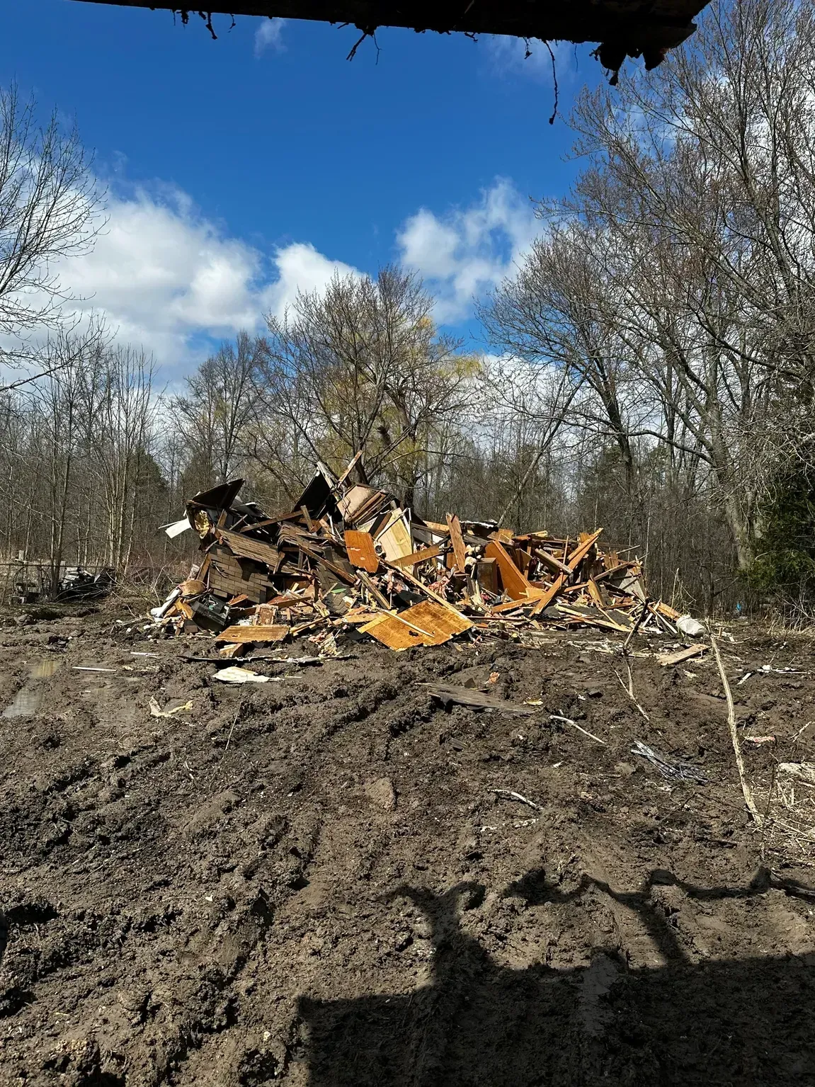 Burned debris pile in a wooded clearing under a blue sky.