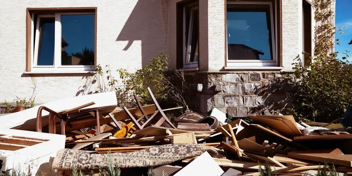 Damaged house exterior with broken windows and a pile of debris and wood in front