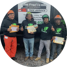 Four workers in safety gear holding certificates in front of a Fred’s Free Service sign