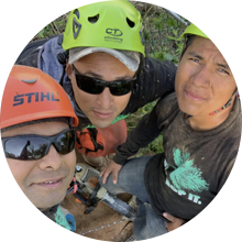 Four climbers in helmets and sunglasses huddle together, taking a selfie outdoors.