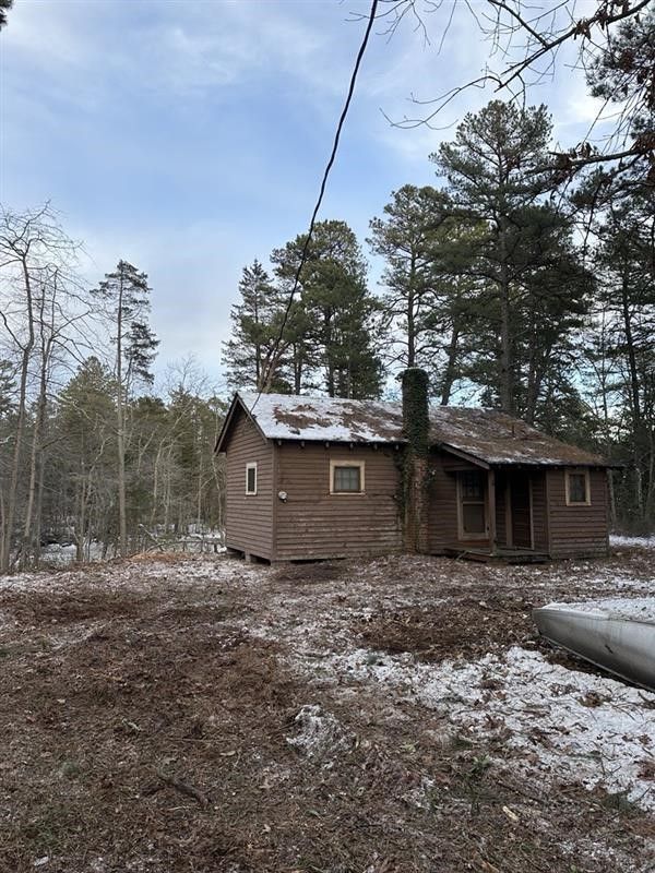 Small rustic log cabin in a snowy pine forest under a cloudy winter sky.