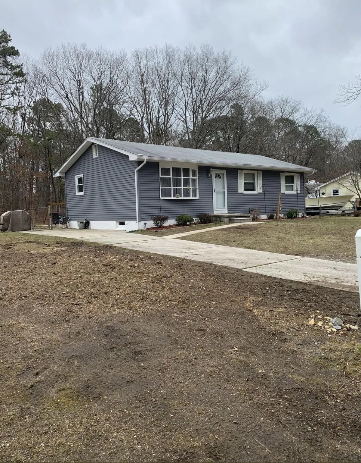 Blue single-story house with white trim and a concrete driveway in a wooded yard