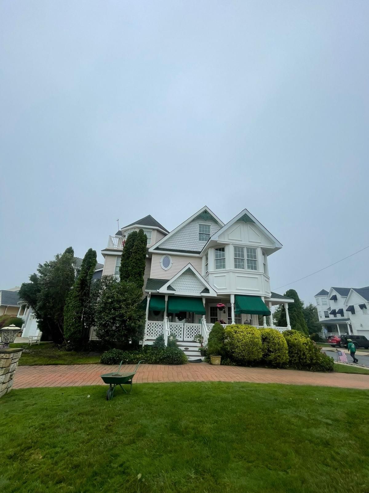 White Victorian-style house with green awnings behind a wet lawn and brick walkway on an overcast day