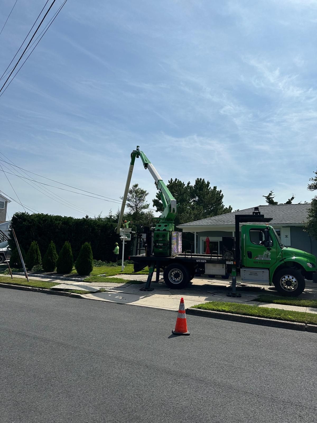 Utility truck with raised boom parked by a curb, with orange cone on a sunny residential street