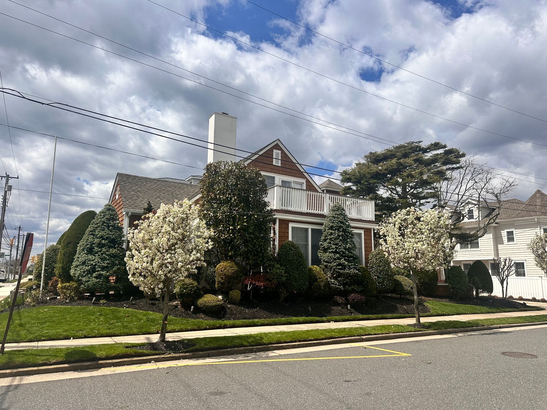 Brick house with white trim and lush front garden on a suburban street under cloudy skies