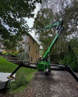 Green boom lift beside a beige house on a gravel driveway under trees