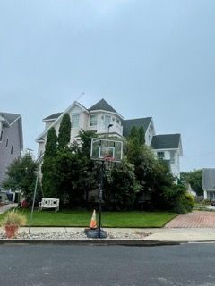 Two-story suburban house with white trim, green roof, and lush front yard under a cloudy sky
