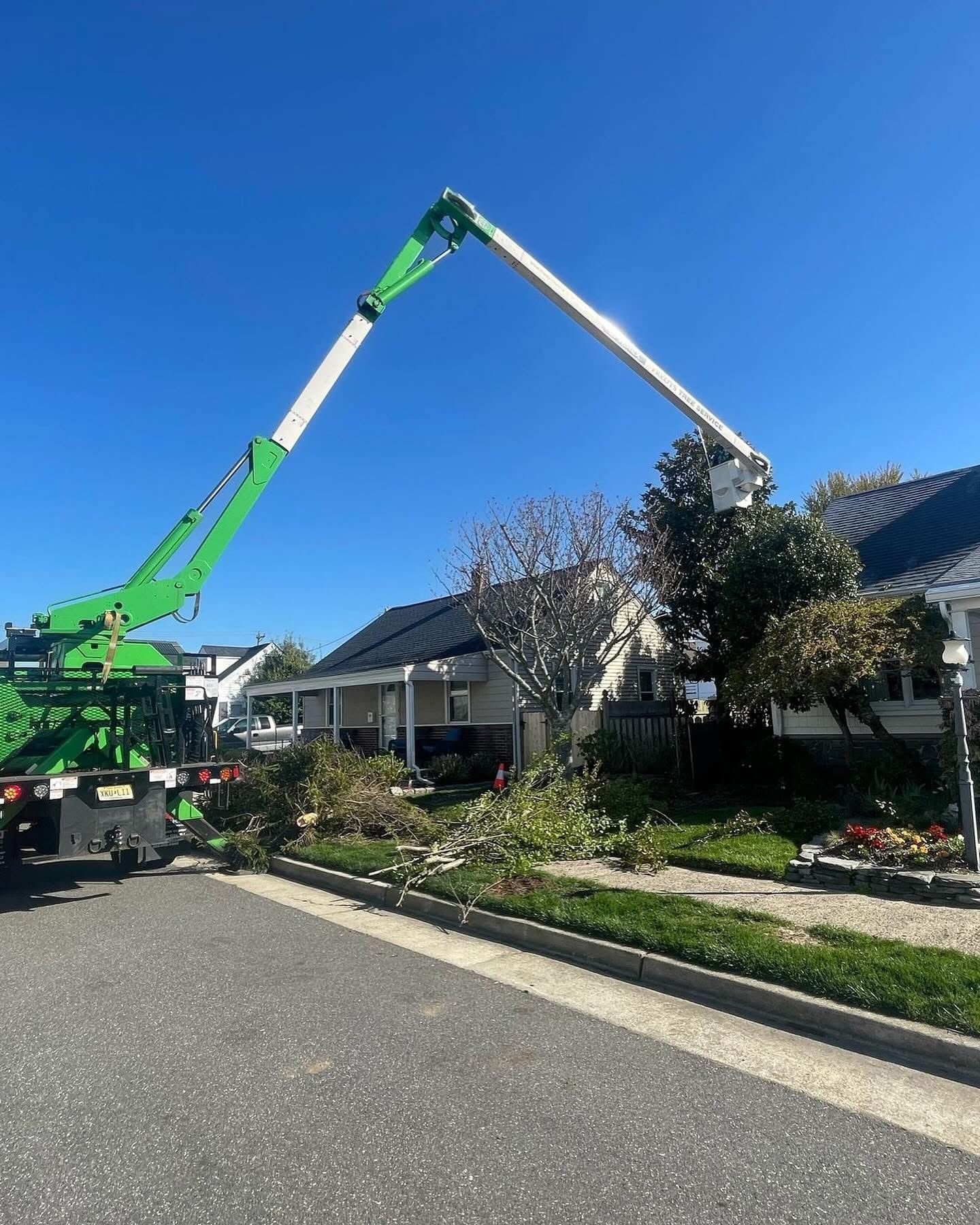 Two green boom lifts extend over a house roof in a sunny suburban street