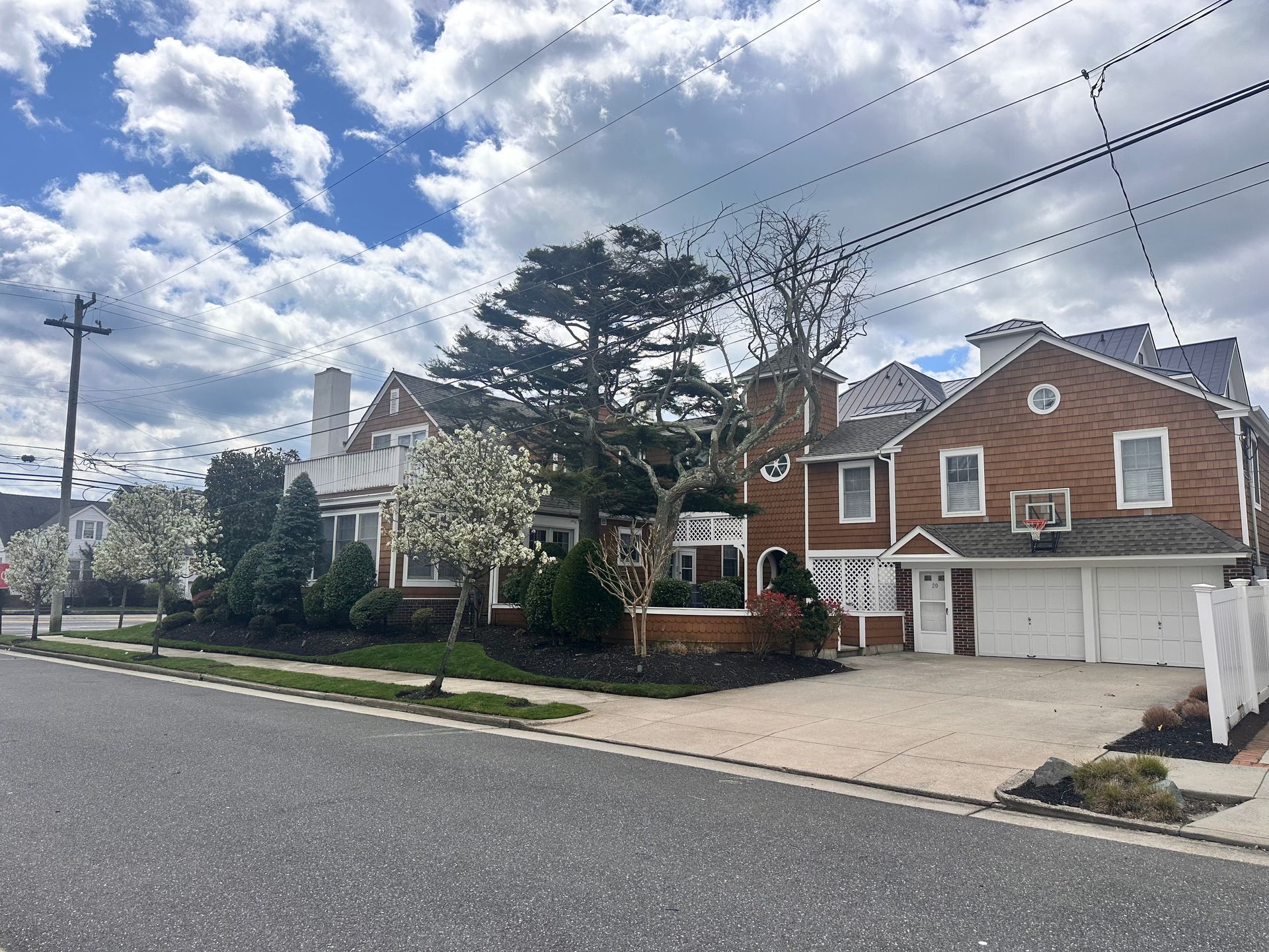 Suburban street with brick houses, driveway, trees, and cloudy sky