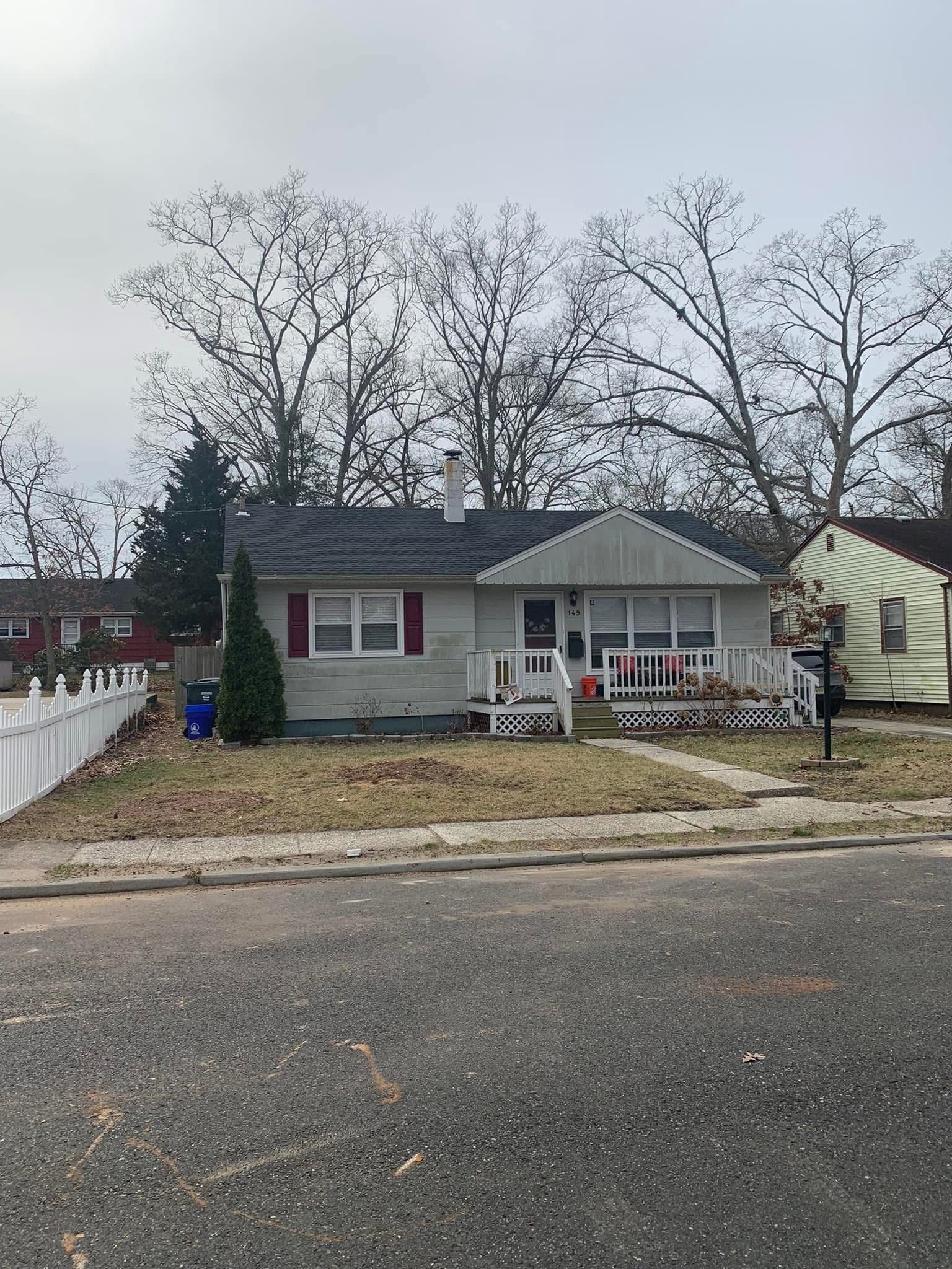 Single-story house with a small front porch, white fence, and bare trees on a cloudy day.