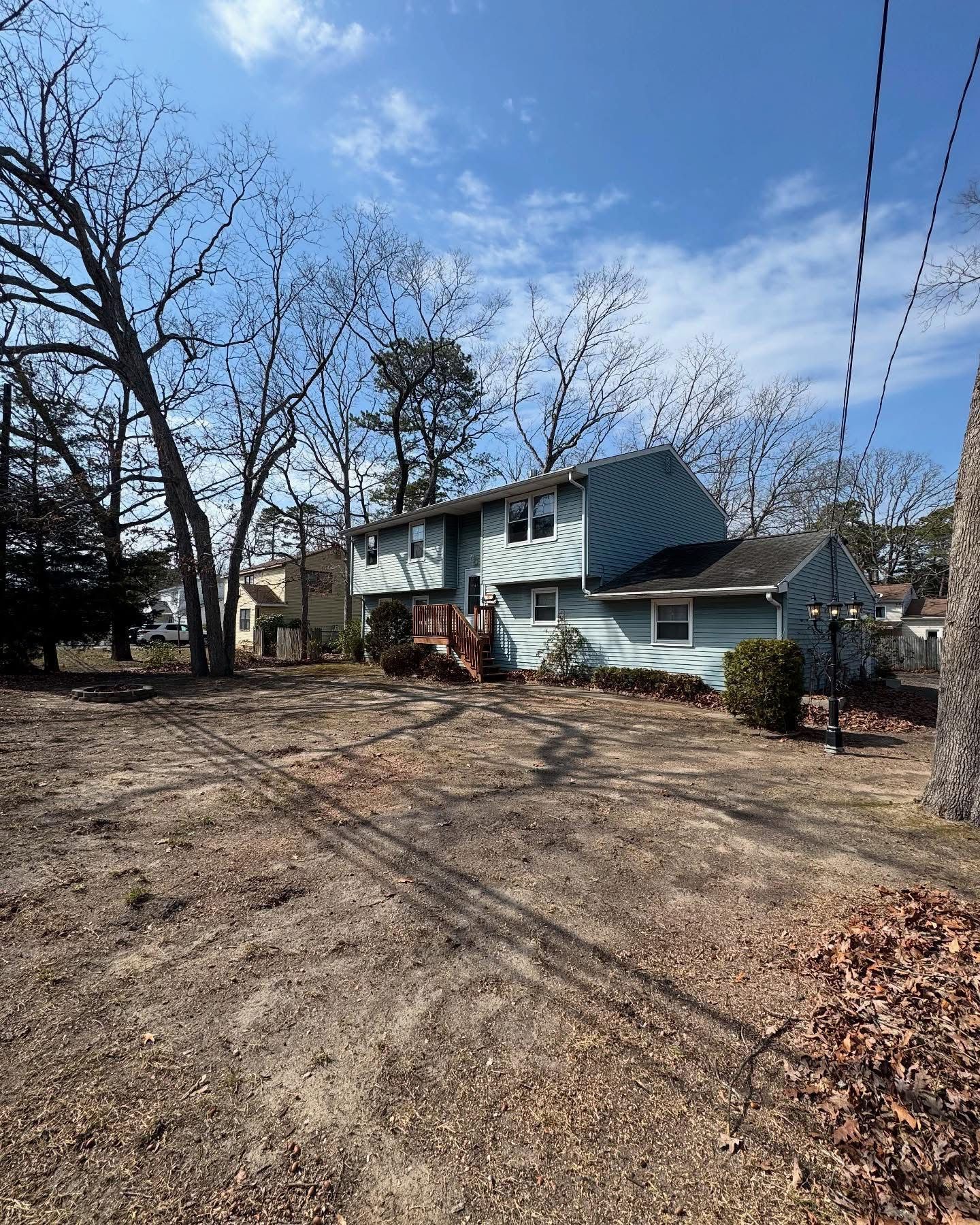 Bare yard with leafless trees beside a blue two-story house under a clear sky.
