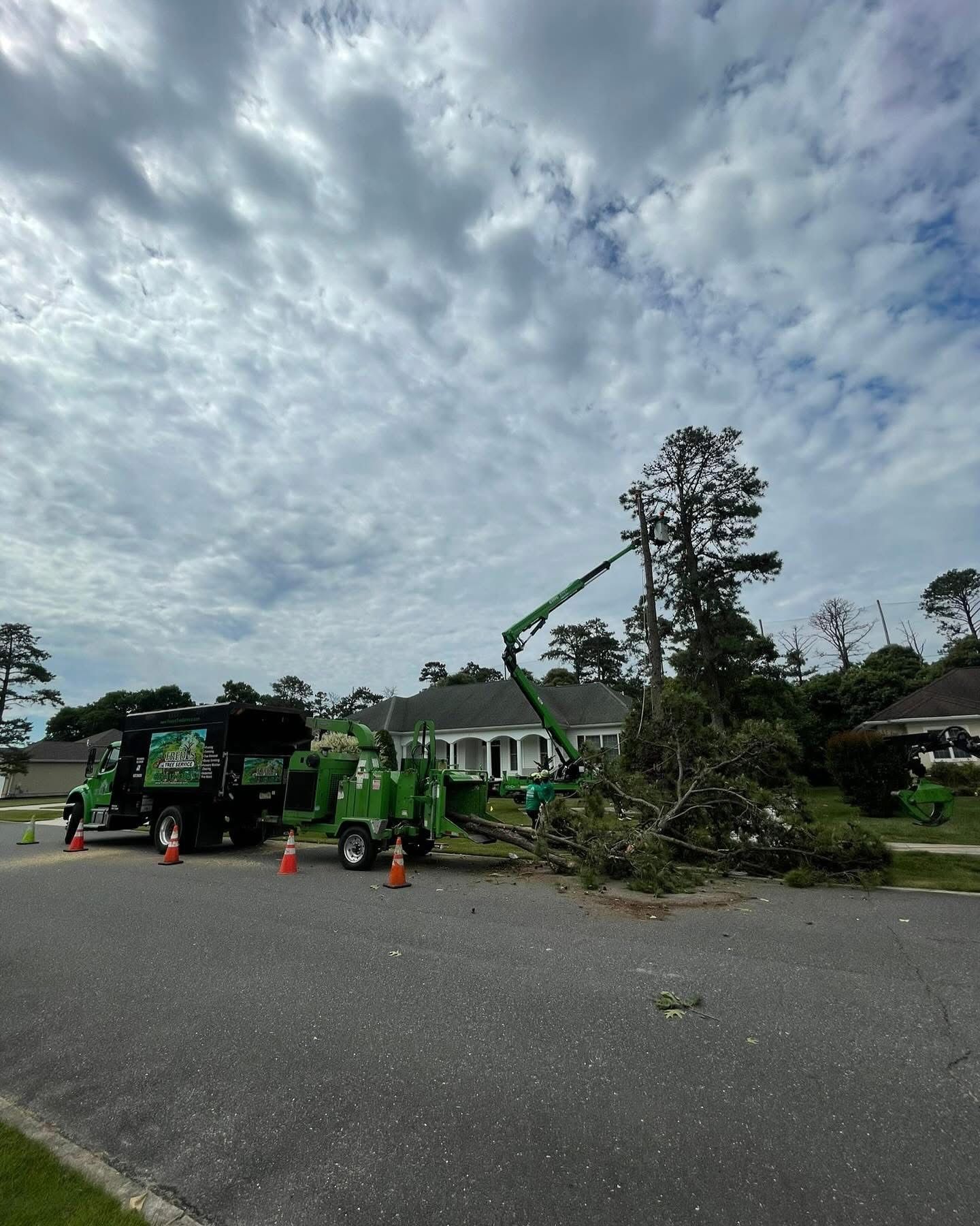 Tree removal truck and workers clearing storm debris on a residential street under cloudy skies