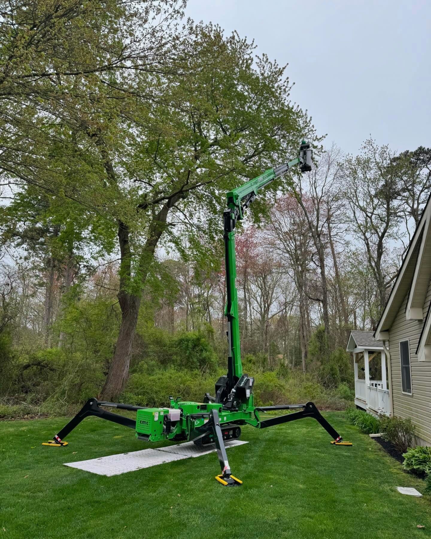 Green spider lift with extended boom on a lawn beside a house and trees