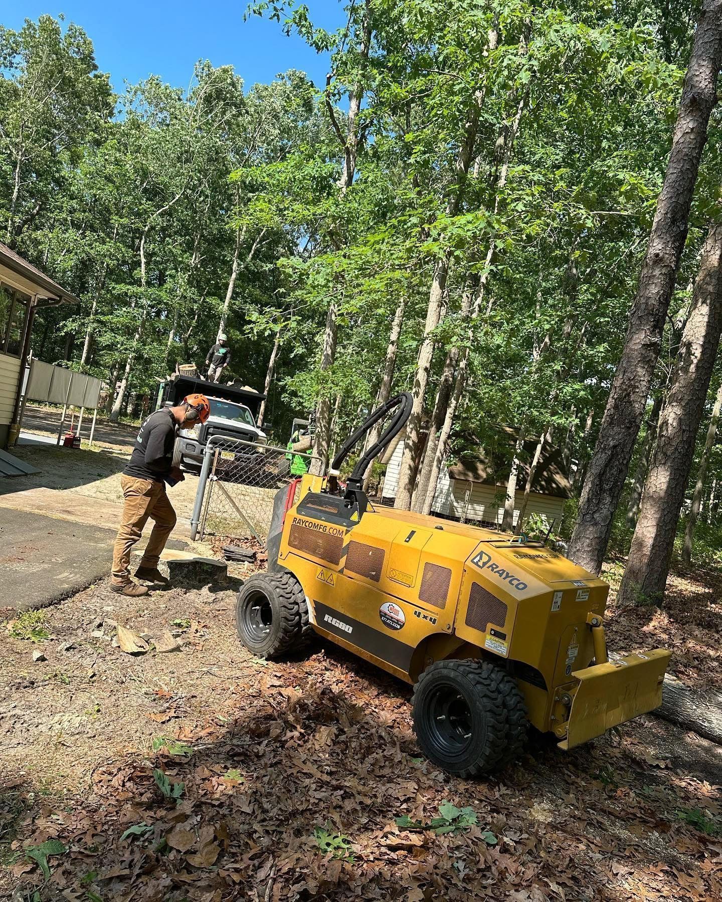 Worker beside yellow wood chipper in a wooded yard, clearing debris from a driveway