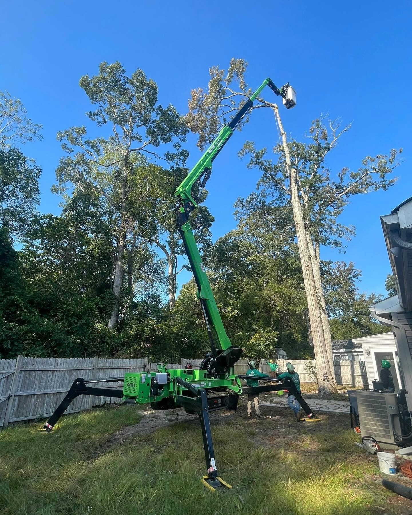 Green crane lifting a tall pole in a grassy yard under a blue sky