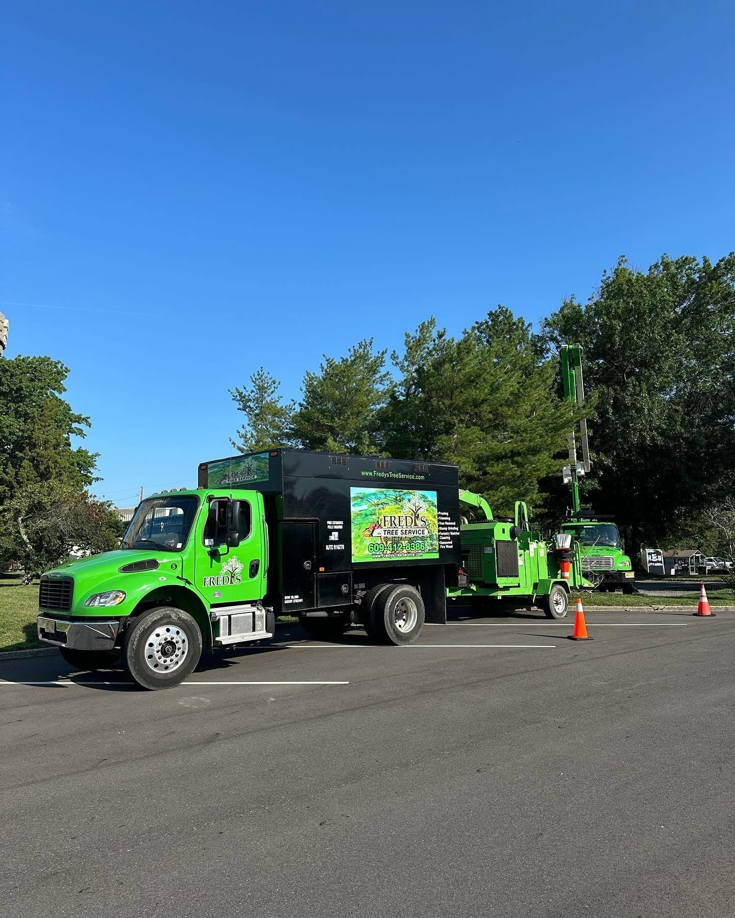 Green utility truck and equipment parked on a road under a clear blue sky, with orange cones nearby.