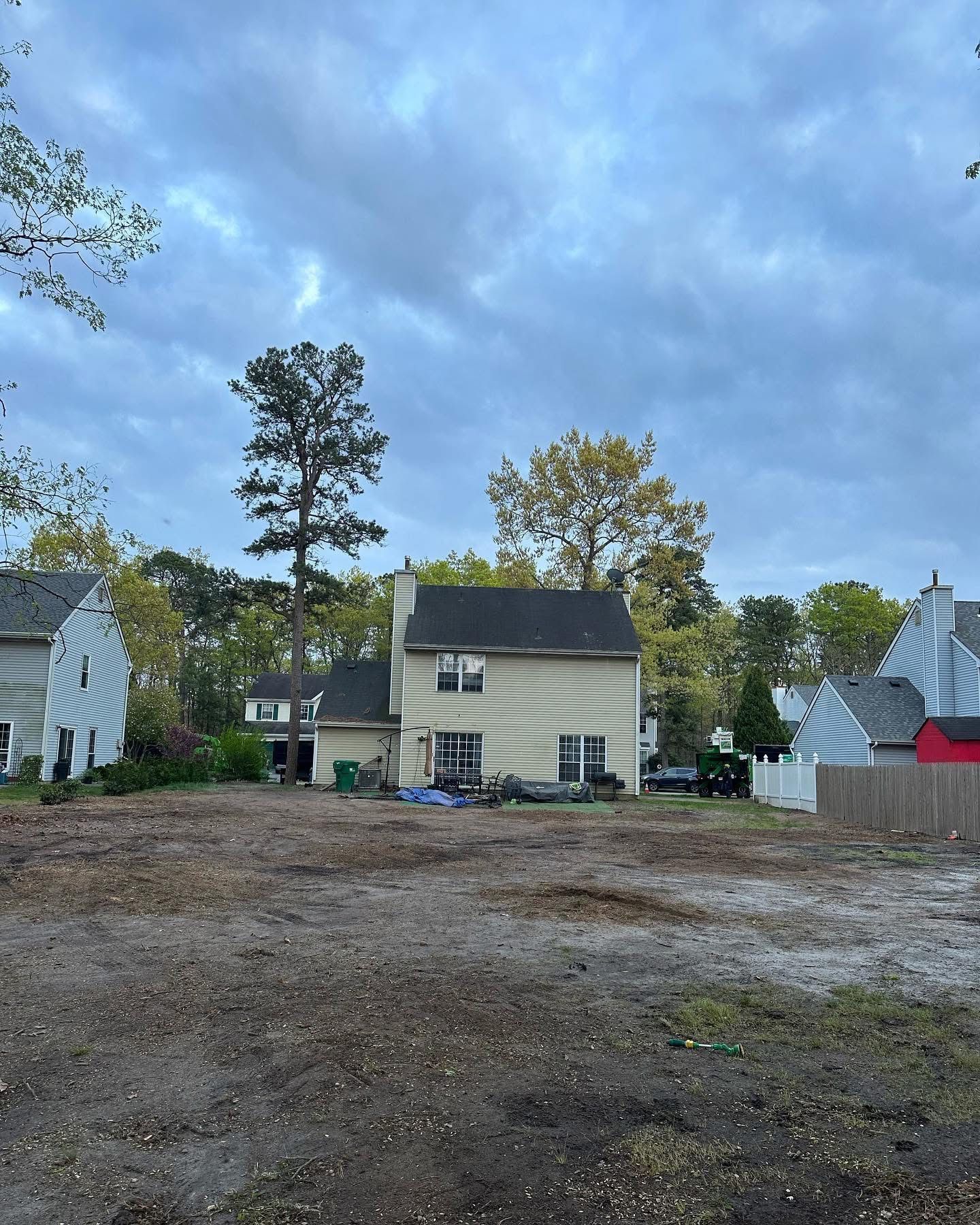 Quiet rural yard with a small beige house, gravel lot, trees, and cloudy sky at dusk