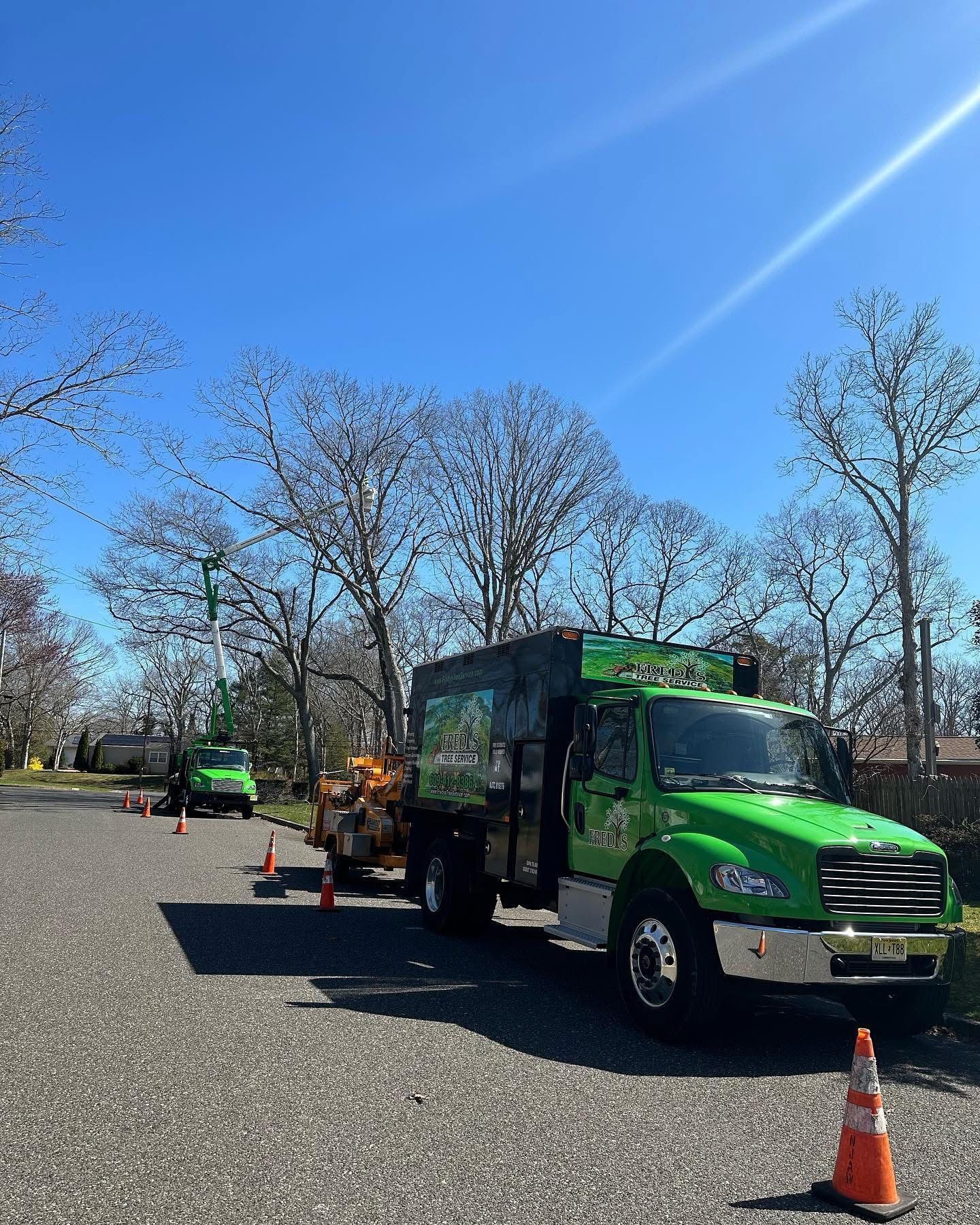 Green utility truck and workers setting up cones on a roadside under a clear blue sky.