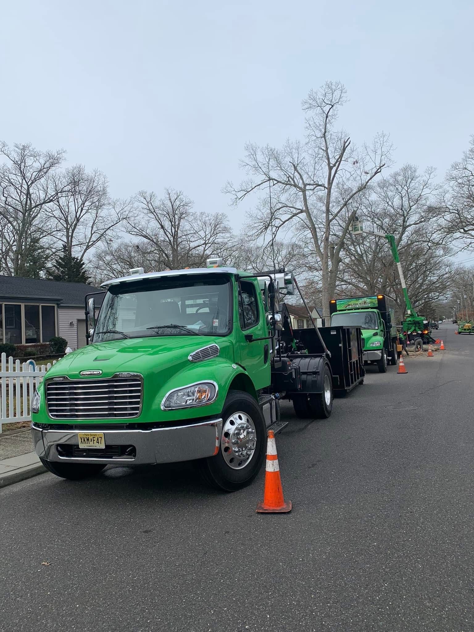 Green utility truck parked on a wet road with orange cones, trees and houses in the background.