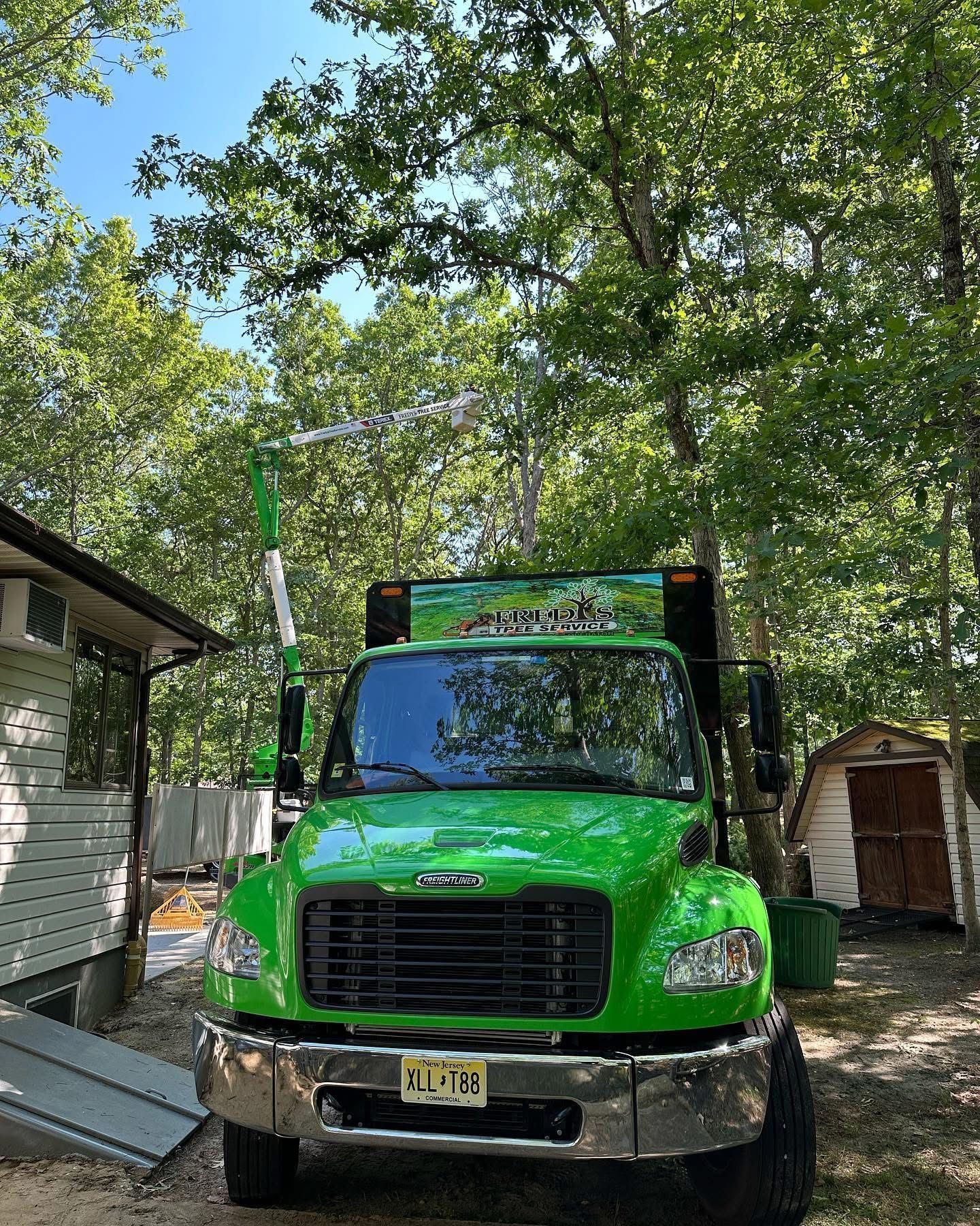 Bright green dump truck parked in a driveway beside a house and trees