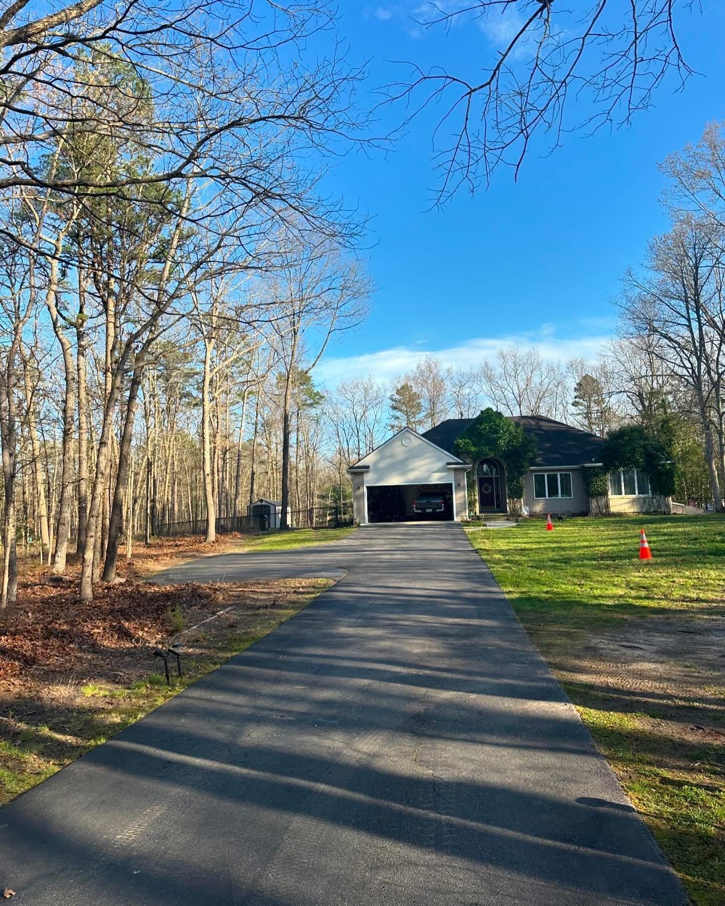 Long driveway leading to a house and garage beside bare trees under a clear blue sky